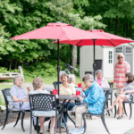 Residents gathered outside at tables under red umbrellas